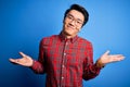 Young handsome chinese man wearing casual shirt and glasses over blue background clueless and confused expression with arms and Royalty Free Stock Photo