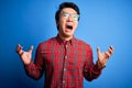 Young handsome chinese man wearing casual shirt and glasses over blue background crazy and mad shouting and yelling with Royalty Free Stock Photo