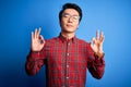 Young handsome chinese man wearing casual shirt and glasses over blue background relax and smiling with eyes closed doing Royalty Free Stock Photo