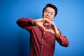 Young handsome chinese man wearing casual shirt and glasses over blue background smiling in love doing heart symbol shape with Royalty Free Stock Photo