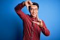 Young handsome chinese man wearing casual shirt and glasses over blue background smiling making frame with hands and fingers with Royalty Free Stock Photo