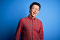 Young handsome chinese man wearing casual shirt and glasses over blue background winking looking at the camera with sexy Royalty Free Stock Photo