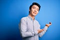 Young handsome chinese man wearing casual shirt standing over isolated blue background Inviting to enter smiling natural with open Royalty Free Stock Photo