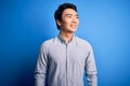 Young handsome chinese man wearing casual shirt standing over isolated blue background looking away to side with smile on face, Royalty Free Stock Photo