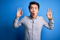 Young handsome chinese man wearing casual shirt standing over isolated blue background looking surprised and shocked doing ok Royalty Free Stock Photo