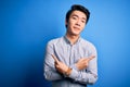 Young handsome chinese man wearing casual shirt standing over isolated blue background Pointing to both sides with fingers, Royalty Free Stock Photo