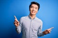 Young handsome chinese man wearing casual shirt standing over isolated blue background smiling confident pointing with fingers to Royalty Free Stock Photo