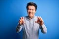 Young handsome chinese man wearing casual shirt standing over isolated blue background smiling funny doing claw gesture as cat, Royalty Free Stock Photo