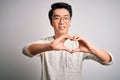 Young handsome chinese man wearing casual t-shirt and glasses over white background smiling in love showing heart symbol and shape Royalty Free Stock Photo