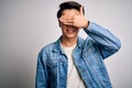 Young handsome chinese man wearing denim jacket and glasses over white background smiling and laughing with hand on face covering Royalty Free Stock Photo