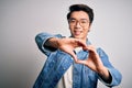 Young handsome chinese man wearing denim jacket and glasses over white background smiling in love doing heart symbol shape with Royalty Free Stock Photo