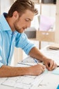 Young handsome confident pensive businessman working sitting at table writing in notebook. White modern office interior Royalty Free Stock Photo