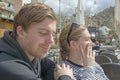 Young handsome couple sit in cafe and squint in stark sunshine