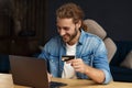 Young handsome curly smiling man with long hair in home office holding credit card and using laptop. Online shopping Royalty Free Stock Photo