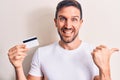 Young handsome customer man holding credit card over isolated white background pointing thumb up to the side smiling happy with Royalty Free Stock Photo