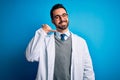 Young handsome doctor man with beard wearing coat and glasses over blue background smiling doing phone gesture with hand and Royalty Free Stock Photo