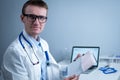 Young handsome doctor man in glasses and white lab coat examines results of electrocardiographic examination of patient Royalty Free Stock Photo