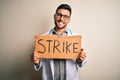 Young handsome doctor man protesting holding cardboard with strike message with a happy face standing and smiling with a confident