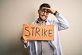 Young handsome doctor man protesting holding cardboard with strike message stressed with hand on head, shocked with shame and