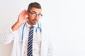 Young handsome doctor man wearing stethoscope over isolated background smiling with hand over ear listening an hearing to rumor or Royalty Free Stock Photo