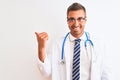 Young handsome doctor man wearing stethoscope over isolated background smiling with happy face looking and pointing to the side Royalty Free Stock Photo