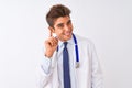 Young handsome doctor man wearing stethoscope over isolated white background smiling with hand over ear listening an hearing to Royalty Free Stock Photo