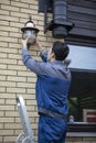 Young handsome electrician standing on ladder and change the light bulb in house facade on the backyard Royalty Free Stock Photo