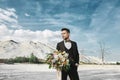 Young handsome elegant man in fashionable suit and bow tie is holding a big bouquet of flowers and looks to side at the Royalty Free Stock Photo