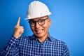 Young handsome engineer latin man wearing safety helmet over isolated blue background pointing finger up with successful idea