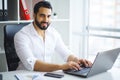 Young handsome entrepreneur sitting at desk and using laptop in