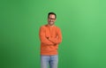 Young handsome entrepreneur standing with arms crossed and smiling at camera on green background