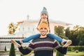 Young handsome father gives piggyback to his little smiling daughter, have fun together when have excursion. Small child looks at Royalty Free Stock Photo