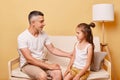 Young handsome father talking with his daughter sitting on cough at home against beige wall having conversation about their Royalty Free Stock Photo