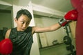 Young handsome and fierce teenager boy doing fight workout punching heavy bag looking cool and badass at fitness club training