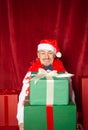 Young handsome funny man wearing Santa hat holding heavy Christmas gift boxes on the red background