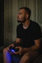 Young handsome gamer man with beard in black t-shirt playing video game using joystick with a concetration on smart face thinking