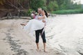 Young handsome groom holds his bride in his arms on the beach with a big bouquet of beautiful flowers Royalty Free Stock Photo