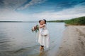 Young handsome groom holds his bride in his arms on the beach with a big bouquet of beautiful flowers Royalty Free Stock Photo