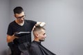 Handsome guy has a haircut in a barbershop, a Kazakh barber dries a client`s hair dryer against a gray wall, a hairdresser makes