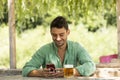 Young, handsome guy in the middle of summer sitting at a table with a beer in nature while looking at his phone smiling Royalty Free Stock Photo