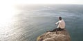 Young handsome guy sitting on rock above ocean