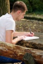 Young handsome guy sitting at wooden table, writing a book, doing homework, taking notes, learning, contemplating and writing. Royalty Free Stock Photo