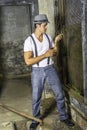 A young handsome guy is standing by a screen window inside a abandoned house,  looking at green leaves and into deeply thinking Royalty Free Stock Photo