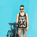 Young handsome guy in sunglasses, a black T-shirt and denim shorts riding a bicycle.on the background of a bright blue wall. Royalty Free Stock Photo