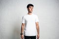 Young handsome guy wearing white blank t-shirt, horizontal studio portrait, empty wall