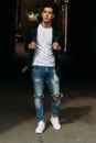 Young, handsome guy in a white T-shirt, black, leather jacket and blue, torn jeans is on the street, model, city walk, live style