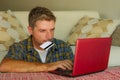 Young handsome and happy man holding credit card sitting at home sofa couch using laptop computer online shopping smiling cheerful Royalty Free Stock Photo