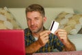 Young handsome and happy man holding credit card sitting at home sofa couch using laptop computer online shopping smiling cheerful Royalty Free Stock Photo