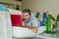 Young handsome happy man lying at home sofa couch working online with laptop computer using netbook relaxed comfortable with beer Royalty Free Stock Photo