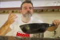 Young handsome and happy man in red apron holding smoking cooking pan smiling cheerful preparing yummy stew smelling delicious